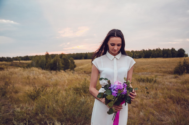 Outdoors portrait of a gorgeous young brunette woman holding lavender flowers. - Photo, image