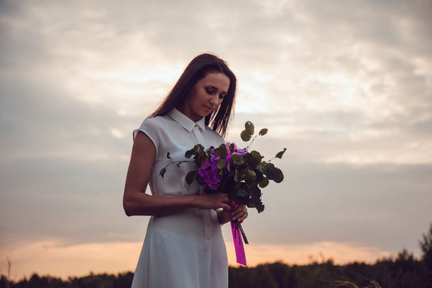 Outdoors portrait of a gorgeous young brunette woman holding lavender flowers. - Zdjęcie, obraz
