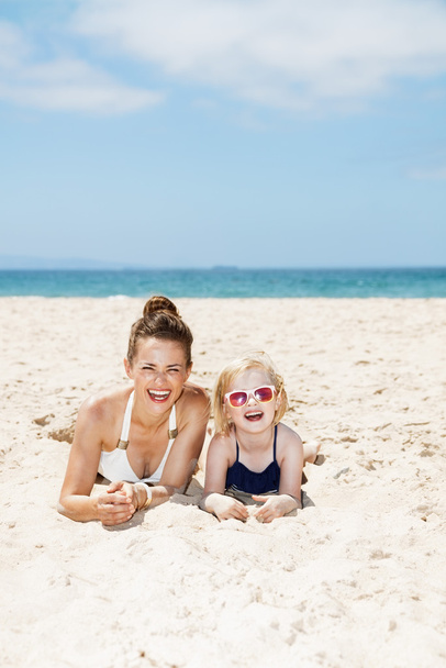 Happy mother and child in swimsuits laying on sandy beach - Photo, Image