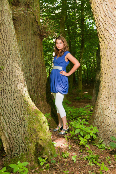 Pretty young woman with long brown hair enjoying nature in forest. Green foliage background. Wearing blue dress. - Foto, Bild