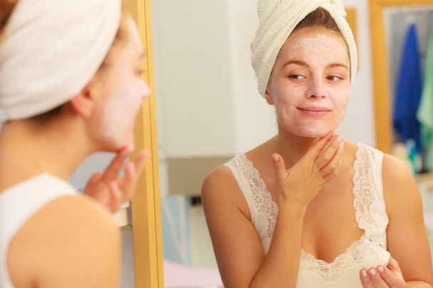 Woman applying mask cream on face in bathroom - Zdjęcie, obraz