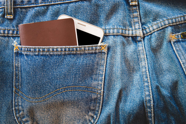 weißes Smartphone und Reisepass oder leeres Notizbuch in der Tasche blaue Jeans. Kopierraum Hintergrund - Foto, Bild