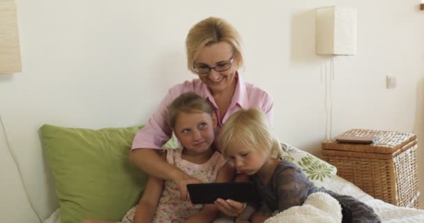Ευτυχισμένη γιαγιά με τα παιδιά που παίζουν παιχνίδια σε tablet στο σπίτι - Πλάνα, βίντεο