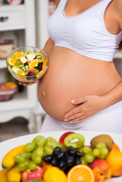 Close-up of a pregnant  tummy with fresh fruit and plate of salad. Healthy pregnancy, diet and vitamins - Foto, imagen