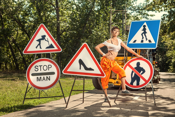Vrouw in oranje overalls is montage "No mannen" borden op de weg - Foto, afbeelding