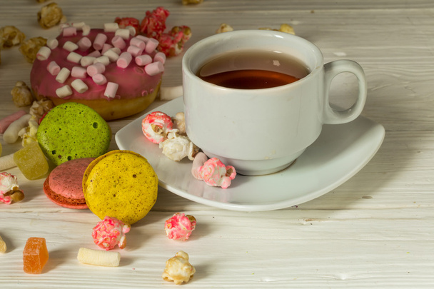Чашка чая на деревянном фоне с пончиком из попкорна макарон
 - Фото, изображение