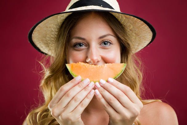 Beautiful young woman in bikini eating melon. Isolated on red. - Фото, изображение