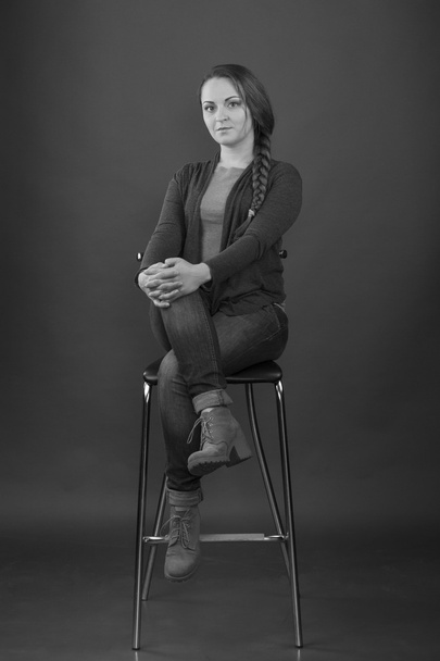 Frau sitzt auf einem Hochstuhl auf grauem Hintergrund. Schwarz-Weiß-Foto - Foto, Bild