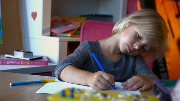 A child with long blond hair is painting something with markers pens, looking away - Foto, Imagem