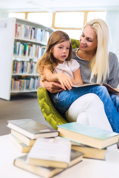 Μητέρα με το κοριτσάκι διαβάσει το βιβλίο μαζί στη βιβλιοθήκη - Φωτογραφία, εικόνα