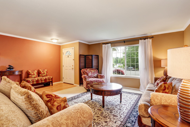 Sala de estar tradicional interior con paredes beige, alfombra y cortinas blancas
 - Foto, Imagen