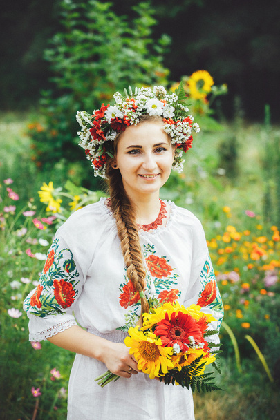 una joven ucraniana en vestido tradicional con un ramo de pie sobre el fondo de flores silvestres
 - Foto, Imagen