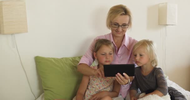 Ευτυχισμένη γιαγιά με τα παιδιά που παίζουν παιχνίδια σε tablet στο σπίτι - Πλάνα, βίντεο