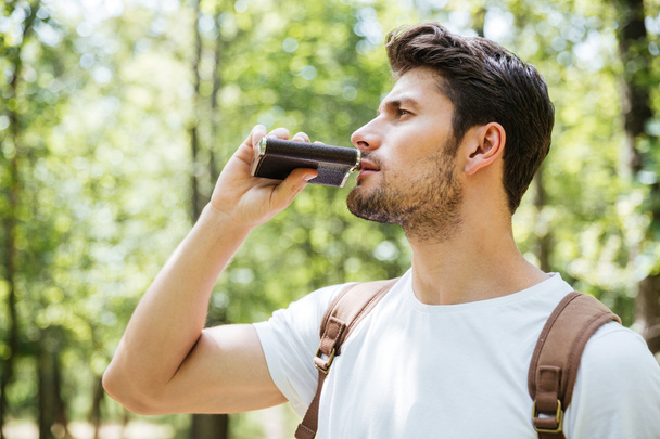 Man with backpack standing and drinking from flask in forest - Foto, Imagen