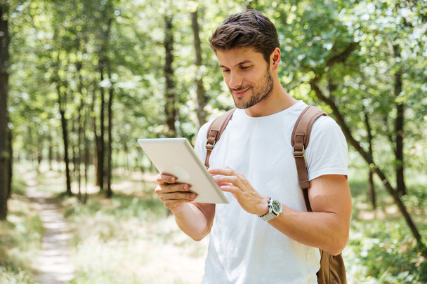 Smiling young man with backpack using tablet in forest - Foto, immagini