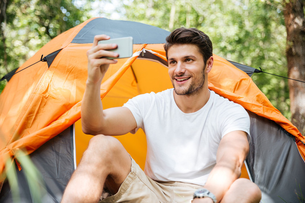 Cheerful man tourist taking selfie with mobile phone in forest - Zdjęcie, obraz
