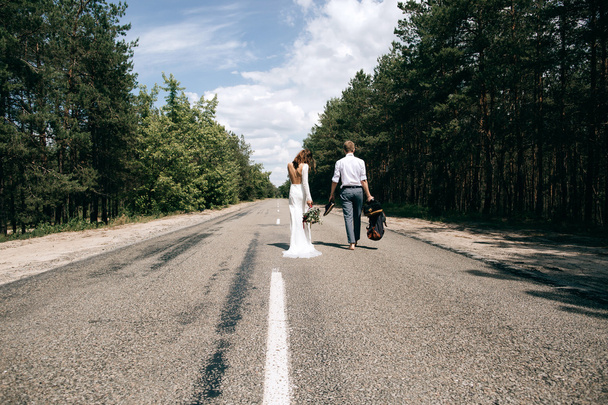 bride and groom walking on the road with a bag - Фото, зображення