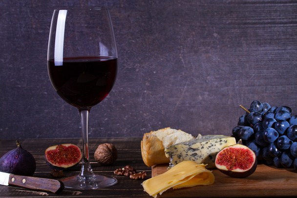 Red wine glass with fruits, cheese, figs and nuts on dark wooden background - Fotó, kép