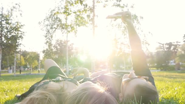 Szczęśliwa Młoda para kochających Dokonywanie selfie z inteligentnych telefonów, leżąc na trawie - Materiał filmowy, wideo