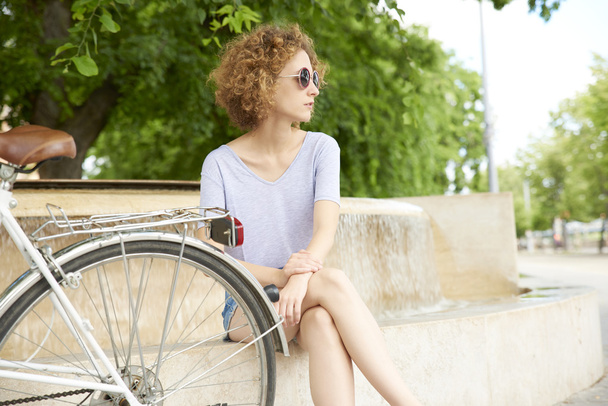 mujer sentada en el parque junto a su bicicleta
 - Foto, Imagen