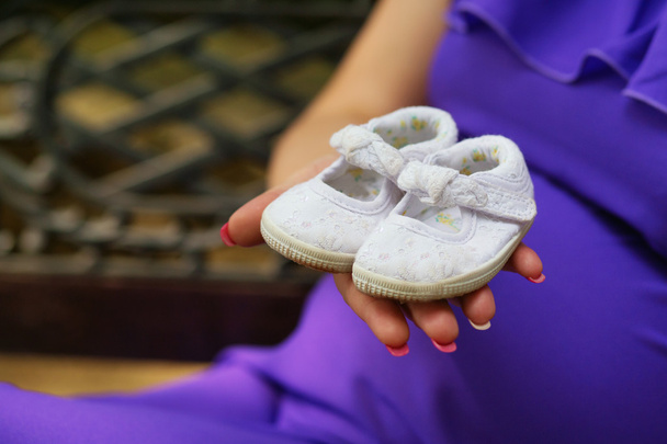 Беременная женщина держит детские туфельки на руке
  - Фото, изображение