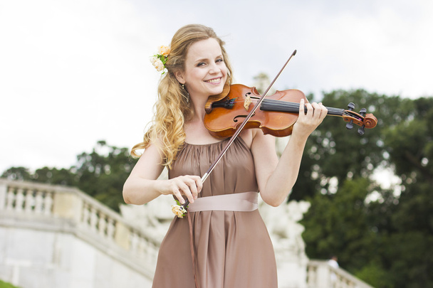 Hermosa chica sonriente tocando en el violín al aire libre. Músico para la boda. Violín bajo el cielo abierto
 - Foto, imagen