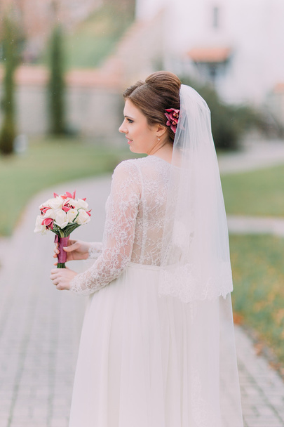 Delicate bride holding bridal bouquet while posing on the park lane at sunny day - Φωτογραφία, εικόνα