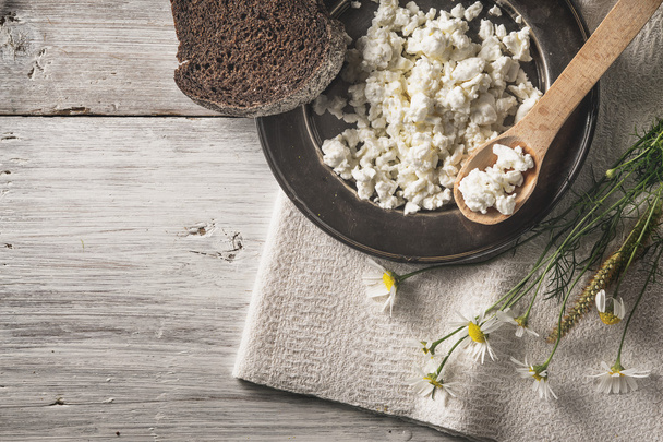 Fresh cottage cheese with bread and flowers on the white wooden table top view - 写真・画像