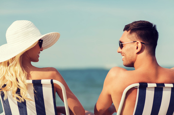 happy couple sunbathing in chairs on summer beach - Zdjęcie, obraz