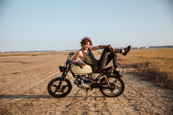 Mladý, brutální muž položil na svém motocyklu a pózování - Fotografie, Obrázek