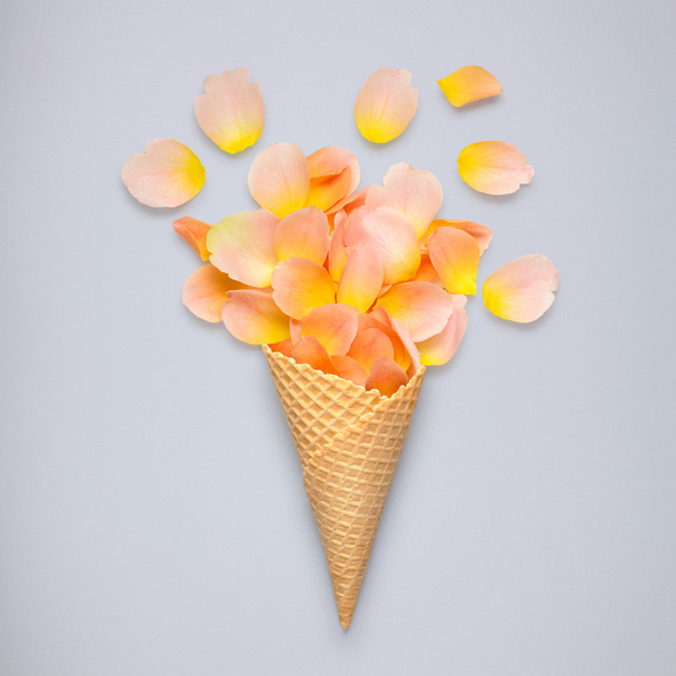 Sweet petals. Creative still life of an ice cream waffle cone with rose petals on grey background. - Фото, зображення