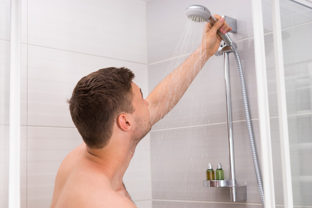 Young man holding shower head with flowing water - Fotó, kép