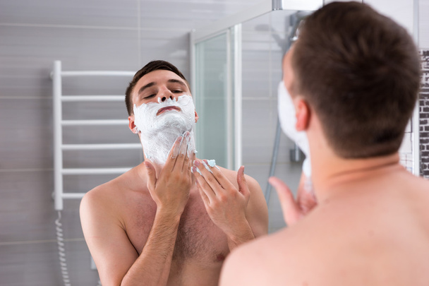 Young man smearing shaving gel on his face - Фото, изображение