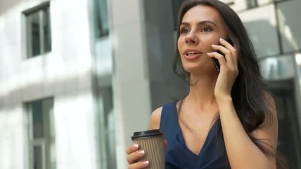Attractive business woman walking in the city, drinking coffee and talking on a phone in the morning - Video