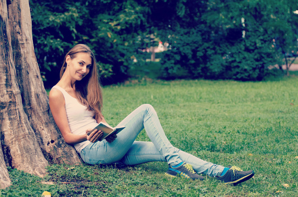 Young woman sitting on the grass and reading book outdoor.  - Fotografie, Obrázek