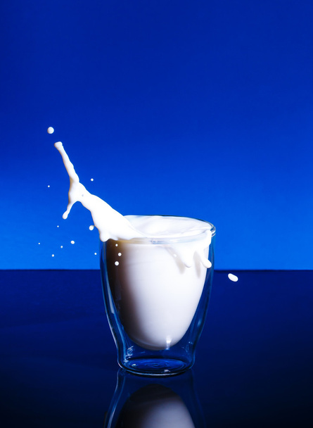 Milk splashing in glass blue background - Foto, Imagen