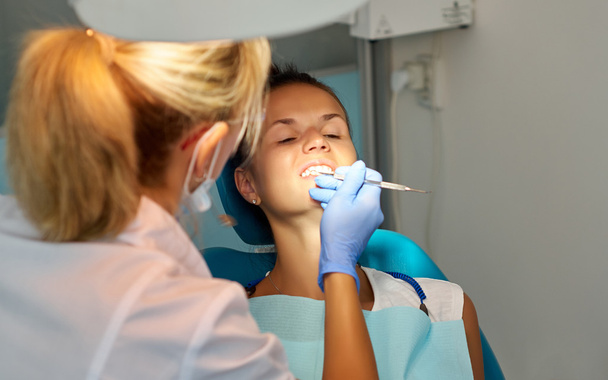 Mooie vrouw tandarts behandeling van een patiënt tanden in tandheelkundige kantoor - Foto, afbeelding