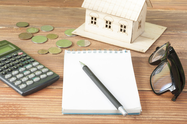 Strona główna oszczędności, koncepcja budżetu. Modelu dom, Notatnik, długopis, kalkulator i monety na stół drewniany office. - Zdjęcie, obraz