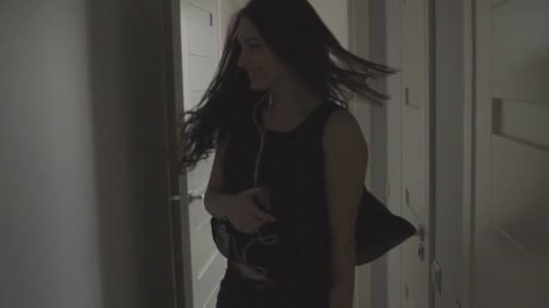 Happy and beautiful brunette girl with earphones dances in her elegant modern apartment - Πλάνα, βίντεο