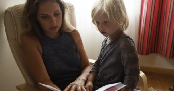 Мати з дитиною дочка сидить у кріслі і читаючи розповідь з картинками. Маленька дівчинка дивиться в книгу і показує пальцем в книзі. - Кадри, відео