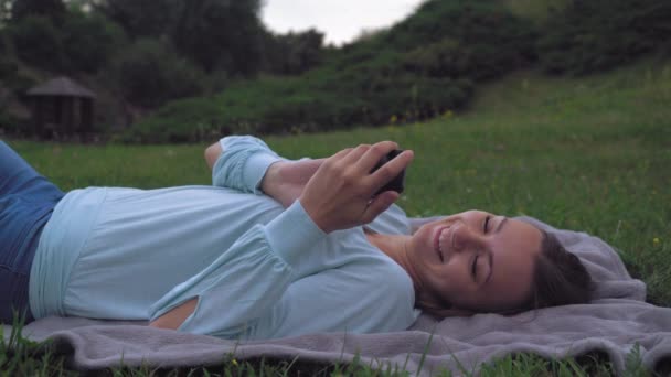 Mladá dívka leží na trávníku v parku, na získání zprávy v telefonu, pak zavře oči a radost dovolené. - Záběry, video