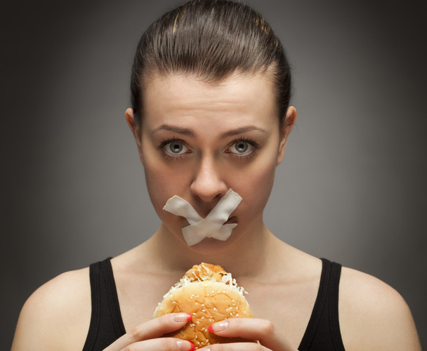 Diet concept: woman holding a burger with mouth sealed - Foto, afbeelding