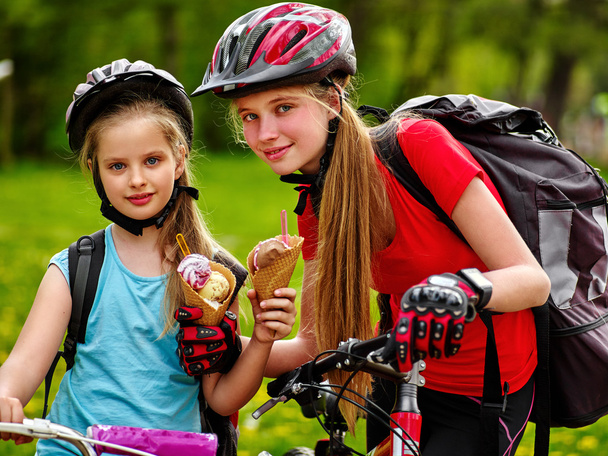 Bicycling girls with rucksack eating ice cream cone in park. - Photo, Image