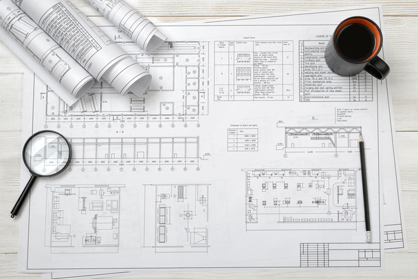 Top view of draftsmans workplace with plan, magnifier, pencil, mug coffee and rolled drafts - Fotografie, Obrázek