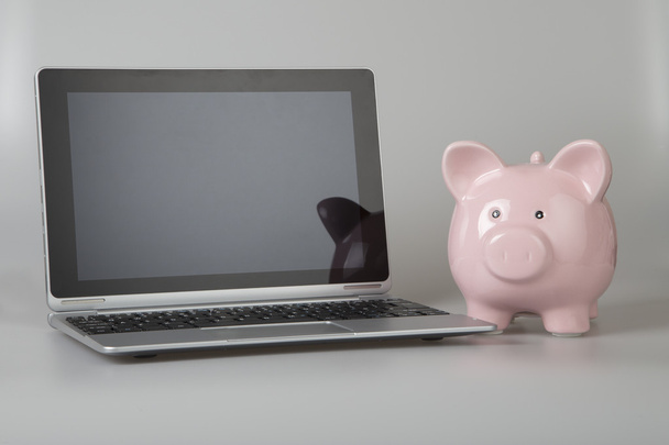 Pink piggy bank next to tablet, laptop - 写真・画像