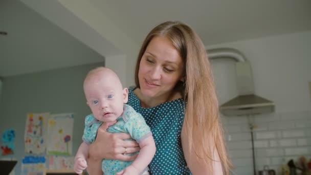 Een close-up van jonge moeders gezicht terwijl ze houdt haar schattige baby geconfronteerd met de camera. Slow Motion - Video