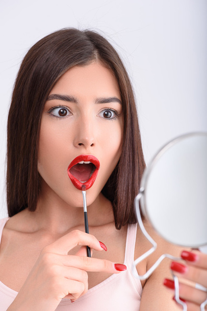 Shocked woman applying red lipstick - Foto, afbeelding