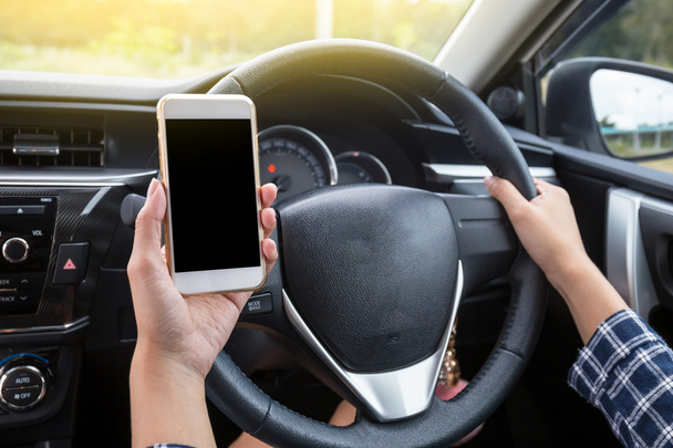Conductora joven usando el teléfono inteligente de pantalla táctil y el volante de mano en un coche
. - Foto, Imagen