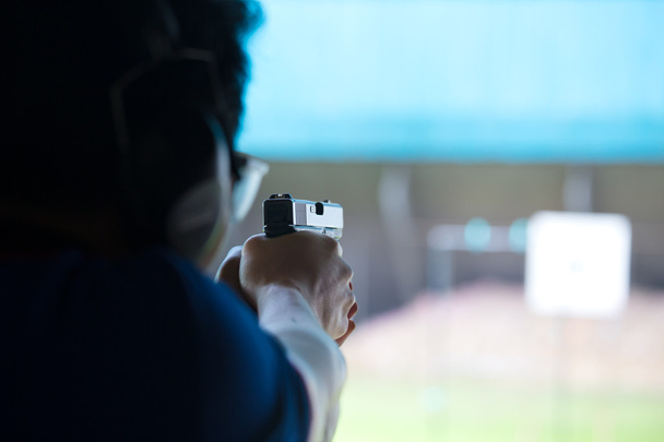 мужчина целился и стрелял из пистолета двумя руками в тире академии
 - Фото, изображение
