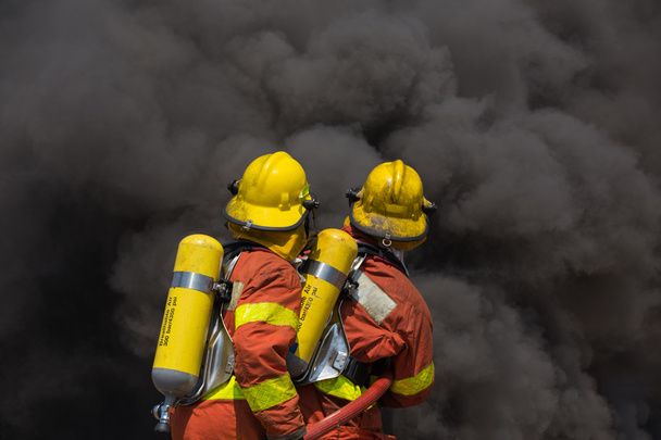 zwei Feuerwehrmänner im Feuerwehranzug treffen auf Feuer und Schwarz  - Foto, Bild